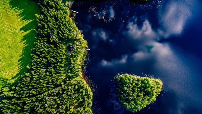 Flygfoto över blå sjö med ö och gröna skogar på en solig sommardag i Finland. Drönarfotografering