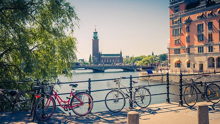 Bikes near bridge railing and Stockholm City Hall (Stadshuset) tower building of Municipal Council and venue of Nobel Prize on Kungsholmen Island, Lake Malaren water on sunny day with blue sky, Sweden